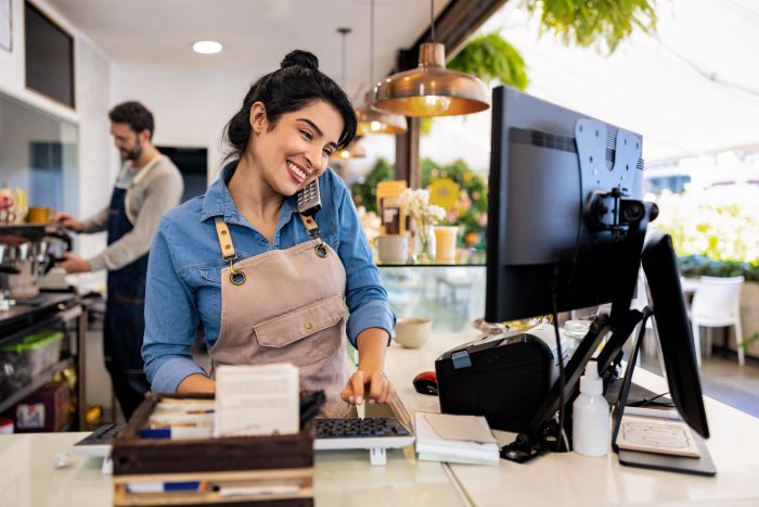A worker at a cafe on the phone and computer at the same time